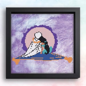May include: Cross-stitch art in a black frame. The artwork depicts two figures embracing on a magic carpet, set against a purple and pink background. The figures are in black and white, with accents of teal and orange.