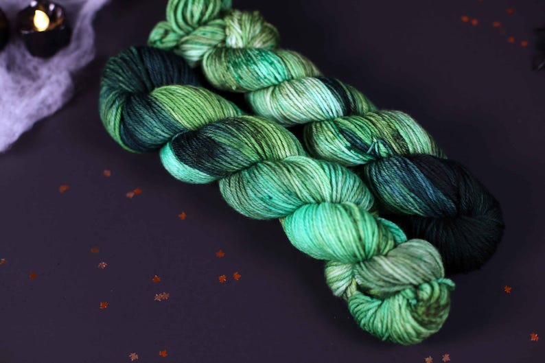 May include: Two skeins of yarn in shades of green and black. The yarn is twisted together and has a variegated colour pattern.