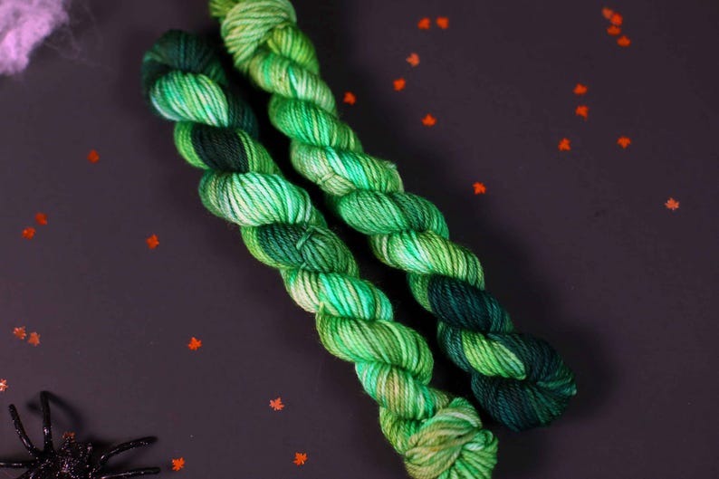 May include: Two skeins of yarn in shades of green and blue. The yarn is twisted together and has a mottled appearance.