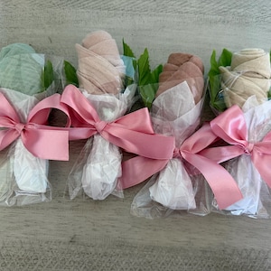 May include: Four fabric rose bouquets, each wrapped in white paper and clear cellophane. The roses are various colors, including light blue, tan, and brown. Each bouquet is tied with a pink satin ribbon.