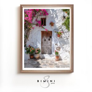 Op de afbeelding: Een witgekalkt gebouw met een houten deur en een raam. Roze bloemen groeien aan een wijnstok die de muur bedekt. Er staan potplanten op de grond en aan de muur.