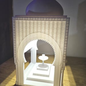 May include: White 3D printed model of a small mosque with a domed roof and intricate details. The mosque has a small fountain inside.