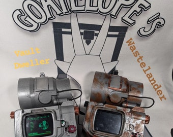 May include: Two wrist-mounted devices with screens, one gray and one rusted, featuring red and black accents. The gray device displays a green interface. The background includes the text "GOATELOPE'S" and "Vault Dweller" and "Wastelander".