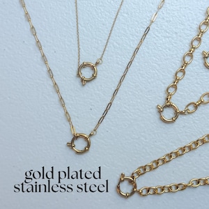 May include: A collection of gold-plated stainless steel necklaces featuring various chain styles, including paperclip and oval links, each equipped with a circular spring ring clasp. The text gold plated stainless steel is visible.