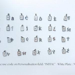 K&ouml;nnte beinhalten: Eine Sammlung von silberfarbenen Metall-Initialen-Anh&auml;ngern, jeweils mit einer rechteckigen wei&szlig;en Platte mit schwarzem Buchstaben oder einem einzelnen Metallbuchstaben-Anh&auml;nger. Der Text unten lautet: Please use code on Personalisation field: INITIAL - White Plate / Metal.