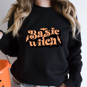 May include: A black sweatshirt with the text "Basic Witch" in orange lettering. The text is in a retro font and is surrounded by small bat silhouettes.