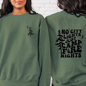 K&ouml;nnte beinhalten: Ein gr&uuml;ner Pullover mit einem schwarzen Design auf der R&uuml;ckseite, das "No City Lights Just Camp Fire Nights" sagt. Die Vorderseite des Pullovers hat ein kleines schwarzes Baumdesign.