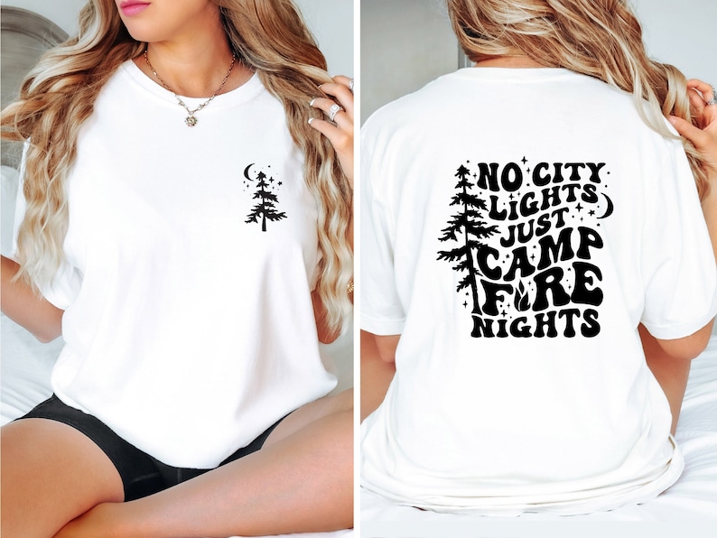 K&ouml;nnte beinhalten: Wei&szlig;es T-Shirt mit einer schwarzen Silhouette eines Kiefernbaums und dem Text "No City Lights Just Camp Fire Nights" auf der R&uuml;ckseite.