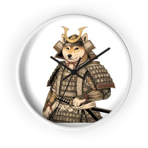 Op de afbeelding: Een ronde wandklok met een witte lijst. De wijzerplaat toont een Shiba Inu-hond in samoerai-pantser, met een katana. De hond is bruin en het pantser is bruin en goud.
