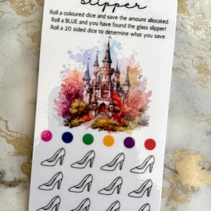 May include: A white rectangular savings tracker card titled The Glass Slipper with a watercolour castle illustration. It features instructions for rolling dice, six coloured circles, and twelve black outline icons of high-heeled shoes.