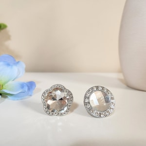 Könnte beinhalten: Zwei silberfarbene Ringe mit klaren Kristallsteinen. Ein Ring hat eine blumenförmige Fassung, der andere eine runde Fassung.