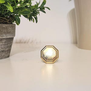 May include: A gold-colored octagonal cabinet knob with a smooth, shiny surface.