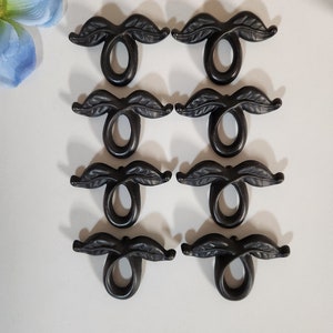 Könnte beinhalten: Acht schwarze,  holzgeschnitzte Vorhangbinder in Form eines Schnurrbartes mit einem Ring in der Mitte.