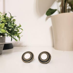 May include: Two round, white, decorative cabinet knobs with a gold and black trim.