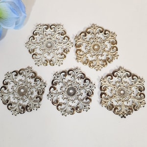 Puede incluir: Cinco adornos decorativos de metal filigranado en oro y blanco con un diseño circular. Los adornos tienen un diámetro de aproximadamente 5 cm.