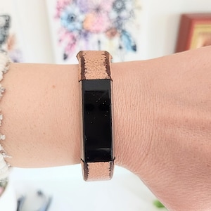 Può includere: Un braccialetto nero e oro rosa è indossato al polso. Il braccialetto ha un centro rettangolare nero con accenti oro rosa nella parte superiore e inferiore. Il polso è di carnagione chiara e la persona indossa un maglione bianco.