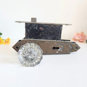Peut inclure: Une ancienne serrure de porte avec un bouton en verre clair et facetté. Le mécanisme de verrouillage est en métal vieilli avec un boîtier rectangulaire foncé et un trou de serrure. Des fleurs décoratives sont en arrière-plan.