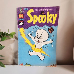 以下が含まれることがあります： 幽霊のキャラクター「Spooky」が描かれた、ビンテージなコミックの表紙。表紙は青と紫で、黄色の稲妻が描かれている。「the tuff little ghost」と「Spooky」の文字が白で印刷されている。