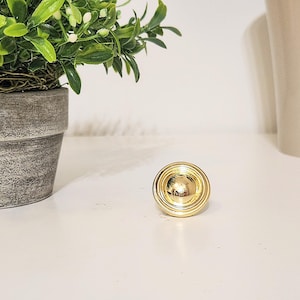 May include: A gold-toned round cabinet knob with a raised centre and concentric circles.