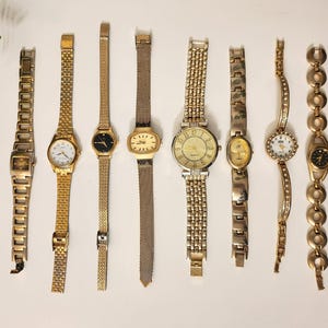 Könnte beinhalten: Eine Sammlung von acht Vintage-Armbanduhren in Goldoptik. Die Uhren variieren im Stil, darunter Gliederarmbänder, Mesh-Armbänder und zarte Kettenarmbänder. Einige haben runde Zifferblätter, andere ovale oder rechteckige.
