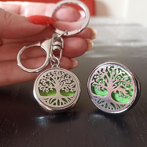 May include: A silver key chain with a round, silver charm featuring a green tree of life design. The charm has a removable top for adding essential oils.