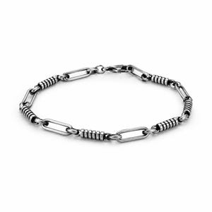 May include: A silver-toned metal chain bracelet featuring alternating elongated oval links and cylindrical segments with horizontal grooved detailing. The bracelet is secured with a small lobster claw clasp, showcasing a polished finish with darkened accents in the grooves.
