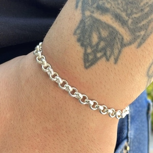 May include: A silver bracelet with a chain link design. The bracelet is made of a shiny, metallic material and is worn on a wrist. The bracelet is a classic piece of jewelry.