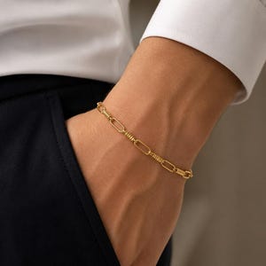 May include: A gold-toned chain bracelet featuring a repeating pattern of elongated oval links alternating with smaller, textured cylindrical segments. The bracelet has a polished finish and a consistent link design throughout its entire length.