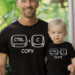 May include: Black t-shirts with white graphics. One shirt displays "CTRL + C COPY", the other "CTRL + V PASTE". The shirts are worn by a father and child, suggesting a matching set or a family theme.