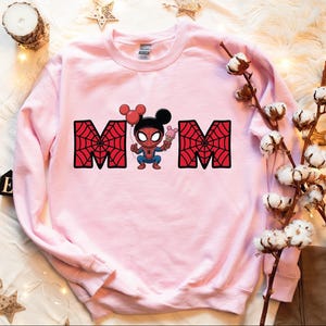 A pink sweatshirt with a Spiderman character printed on it, along with some decorative elements such as a candle, cotton balls, and star-shaped ornaments.