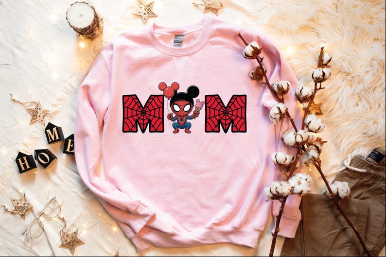 A pink sweatshirt with a Spiderman character printed on it, along with some decorative elements such as a candle, cotton balls, and star-shaped ornaments.