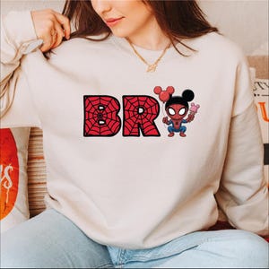 A woman wearing a white sweatshirt with the text "BR" and a Spider-Man character on it.
