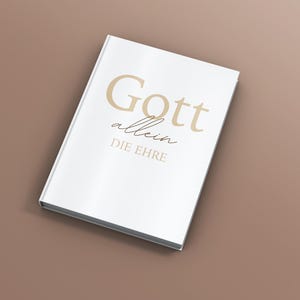 Peut inclure: Un livre blanc avec les mots "Gott allein DIE EHRE" en lettres dorées. Le livre est fermé et incliné sur une surface marron. Le texte est en police serif.