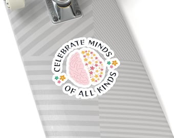 Op de afbeelding: Een ronde sticker met een illustratie van een brein in twee helften: de ene kant is effen lichtroze, de andere kant bestaat uit kleine kleurrijke bloemetjes. De tekst "CELEBRATE MINDS OF ALL KINDS" staat in een boog om het centrale ontwerp.