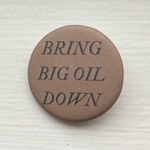 May include: A brown button with the text "BRING BIG OIL DOWN" in black.
