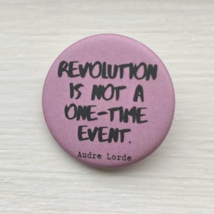 Könnte beinhalten: Ein rosa Knopf mit dem Zitat "Revolution ist kein einmaliges Ereignis." von Audre Lorde.