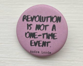 Könnte beinhalten: Ein rosa Knopf mit dem Zitat "Revolution ist kein einmaliges Ereignis." von Audre Lorde.