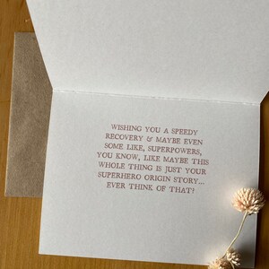 May include: A white card with a pink message wishing someone a speedy recovery. The message says "Wishing you a speedy recovery & maybe even some like, superpowers, you know, like maybe this whole thing is just your superhero origin story... Ever think of that?"