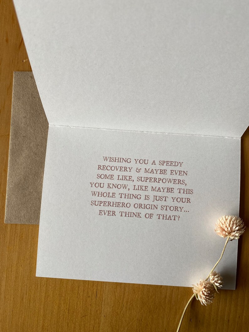 May include: A white card with a pink message wishing someone a speedy recovery. The message says "Wishing you a speedy recovery & maybe even some like, superpowers, you know, like maybe this whole thing is just your superhero origin story... Ever think of that?"