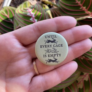 Op de afbeelding: Een groene knop met de tekst "Until every cage is empty" en drie zwarte silhouetten van konijnen die rennen.