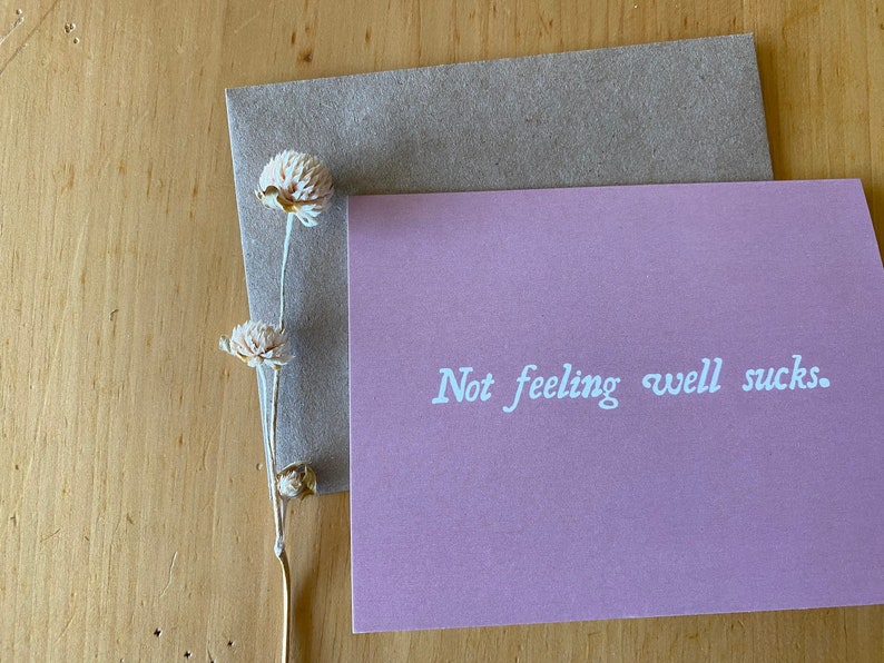 May include: A pink card with the text "Not feeling well sucks." written in white cursive font.