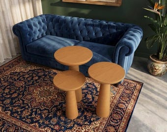 Könnte beinhalten: Ein Set aus drei hellbraunen Holztischen mit runden Tischplatten und konisch zulaufenden zylindrischen Beinen, die in einer Gruppe angeordnet sind. Die Tische haben eine glatte, gleichmäßige Oberfläche und stehen auf einem dunkelblauen Teppich.