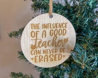 May include: A round wooden ornament with the text "The influence of a good teacher can never be erased" and two red apple icons.