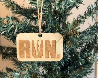 Könnte beinhalten: Ein hölzerner Weihnachtsbaumschmuck mit dem Wort "RUN" und einer Silhouette einer laufenden Figur. Der Schmuck hängt an einem grünen künstlichen Weihnachtsbaum.