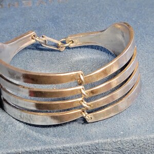 May include: Silver bracelet with four bands and a chain link closure. The bracelet is on a blue background.
