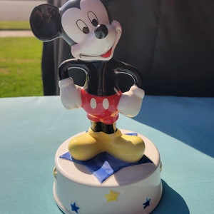 May include: A ceramic Mickey Mouse music box. Mickey is standing on a blue and white star with yellow stars around the base.