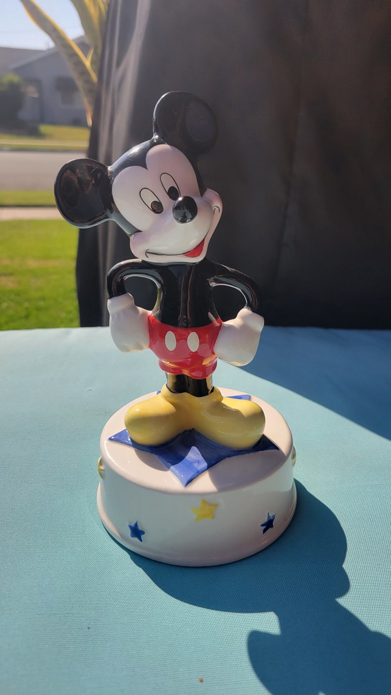 May include: A ceramic Mickey Mouse music box. Mickey is standing on a blue and white star with yellow stars around the base.