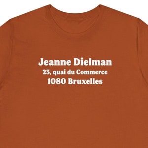 Puede incluir: Una camiseta de color óxido con texto blanco que dice "Jeanne Dielman 23, quai du Commerce 1080 Bruxelles".