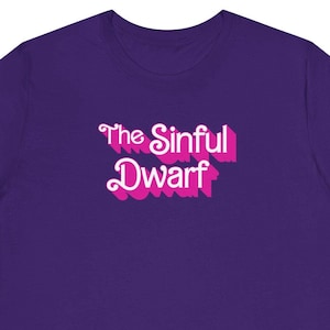 May include: Purple t-shirt with a pink graphic that says "The Sinful Dwarf" in a retro font.
