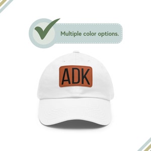 May include: White baseball cap with a brown leather patch that says "ADK" in black letters.